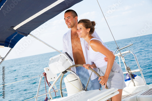 Loving couple steering yacht in calm blue ocean during romantic summer vacation
