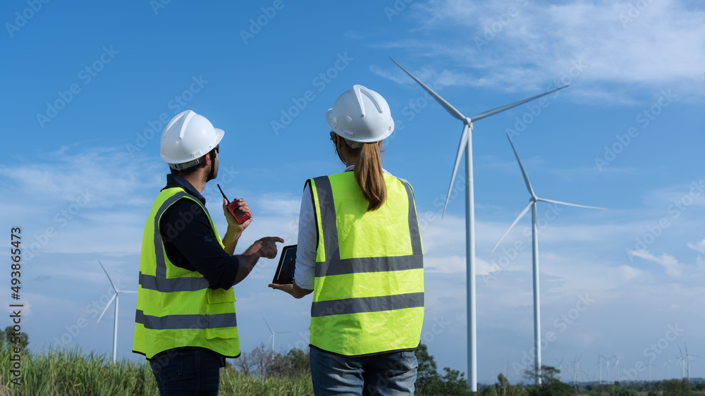 Back view of two engineers discussing against turbines on wind turbine farm. Back view of two engineers discussing against turbines on wind turbine farm.