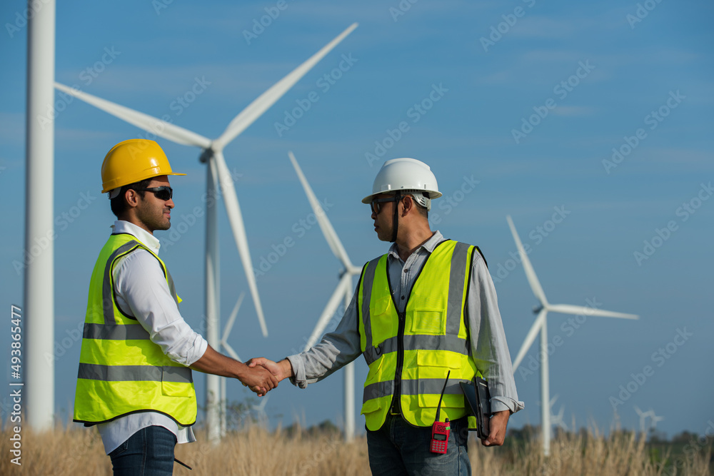 Two engineers working and Handshake at wind turbine farm Power Generator Station on background,Thailand people Two engineers working and Handshake at wind turbine farm Power Generator Station on background,Thailand people