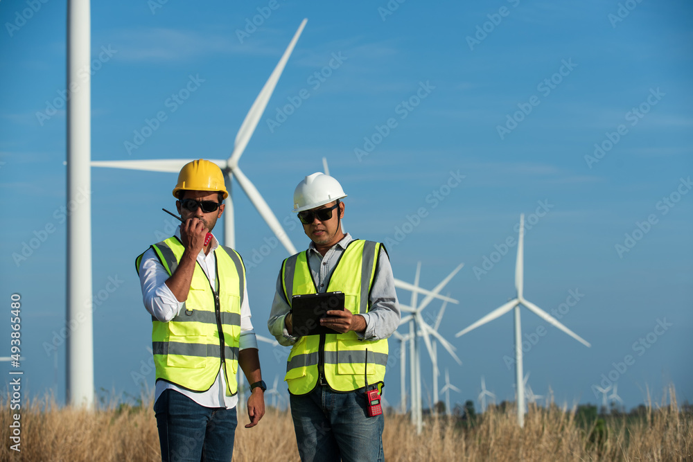 portrait of a worker in a hardhat. Two maintenance engineer in hand holding tablet and radio communication in wind turbine farm on background. portrait of a worker in a hardhat. Two maintenance engineer in hand holding tablet and radio communication in wind turbine farm on background.