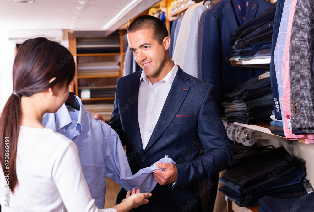 Young happy couple choosing stylish dress shirt for man in modern boutique..