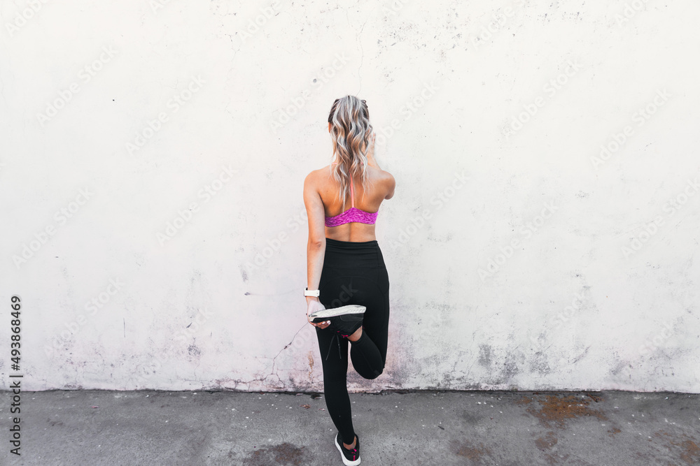 young active sport woman stretching quads on a wall. Home backyard workout. Copy space.
