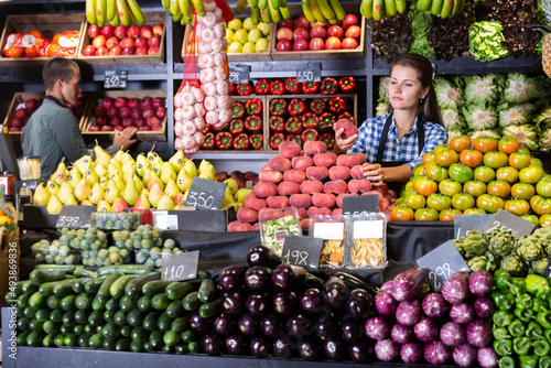 Young woman selling fresh peaches and vegetables on the supermarket..