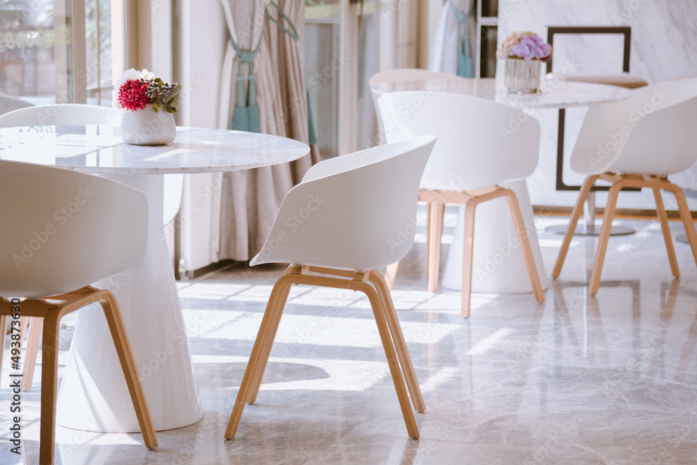 Obraz premium Sunlight streamed through floor-to-ceiling windows into a reception room set with white tables. White minimalist modern dining room interior design.