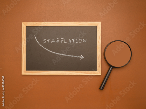 Hand draws an arrow of stagflation with chalk on a blackboard and magnifying glass over a brown background photo