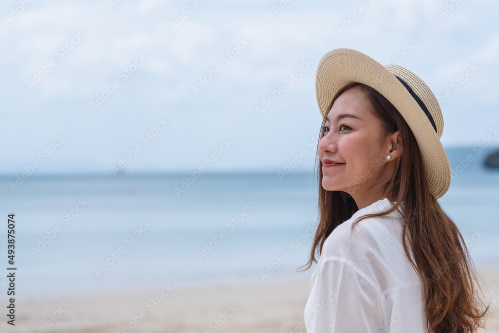 Portrait image of a beautiful young asian woman while strolling on the beach with the sea and blue sky background