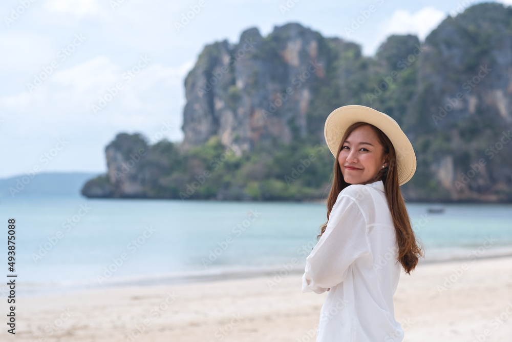 Portrait image of a beautiful young asian woman while strolling on the beach with the sea and blue sky background