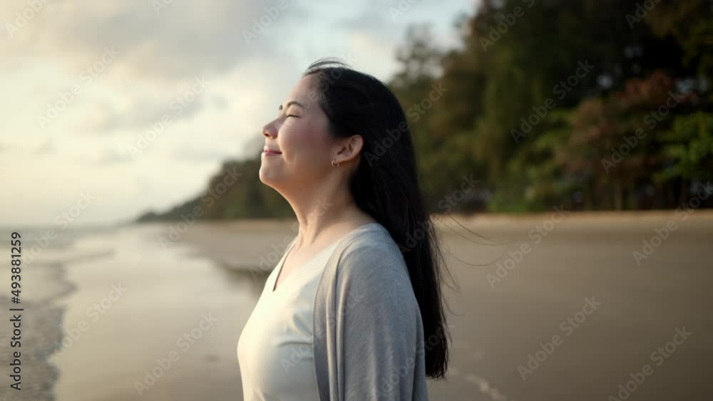 Young asian woman with straw hat standing alone on empty sand beach at sunset seashore. Chilling in holiday weekend summertime. Traveler Female walking around the beach with the sunlight Young asian woman with straw hat standing alone on empty sand beach at sunset seashore. Chilling in holiday weekend summertime. Traveler Female walking around the beach with the sunlight
