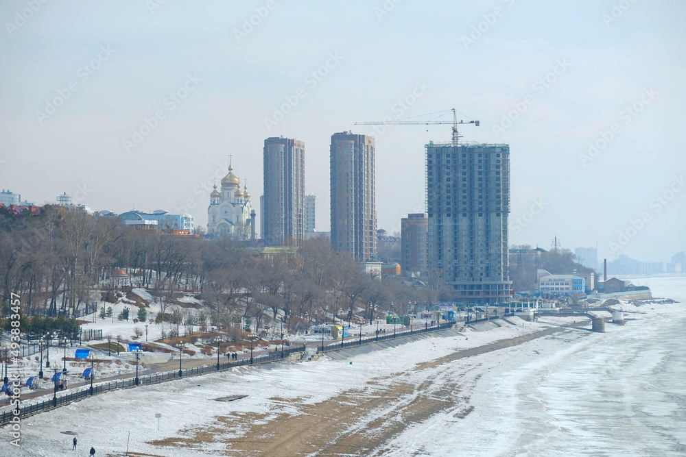 Fototapeta premium Magadan, Russia - 03.24.2018 : The bank of the frozen Amur River on the background of administrative buildings.