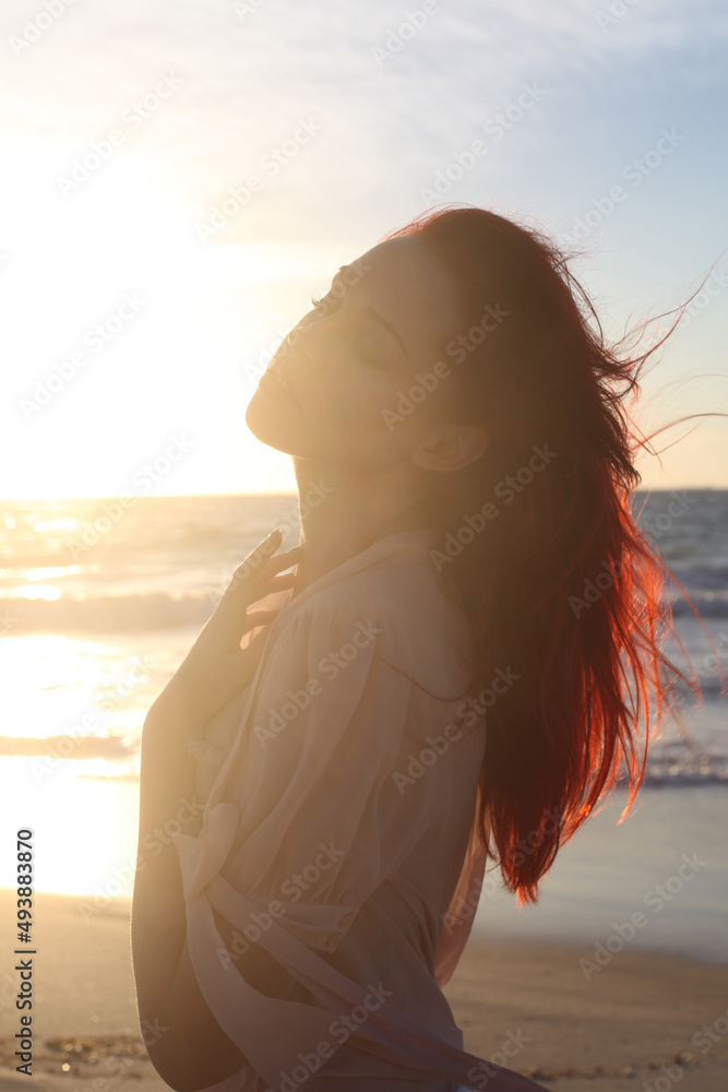 Full length portrait of  red haired woman wearing  torn shipwrecked clothing. Standing  pose with gestural hands at  rocky ocean beach landscape background.
