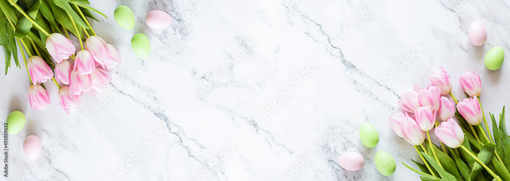 Stylish background with colorful easter eggs isolated on white marble background with pink tulip flowers. Flat lay, top view, mockup, overhead, template