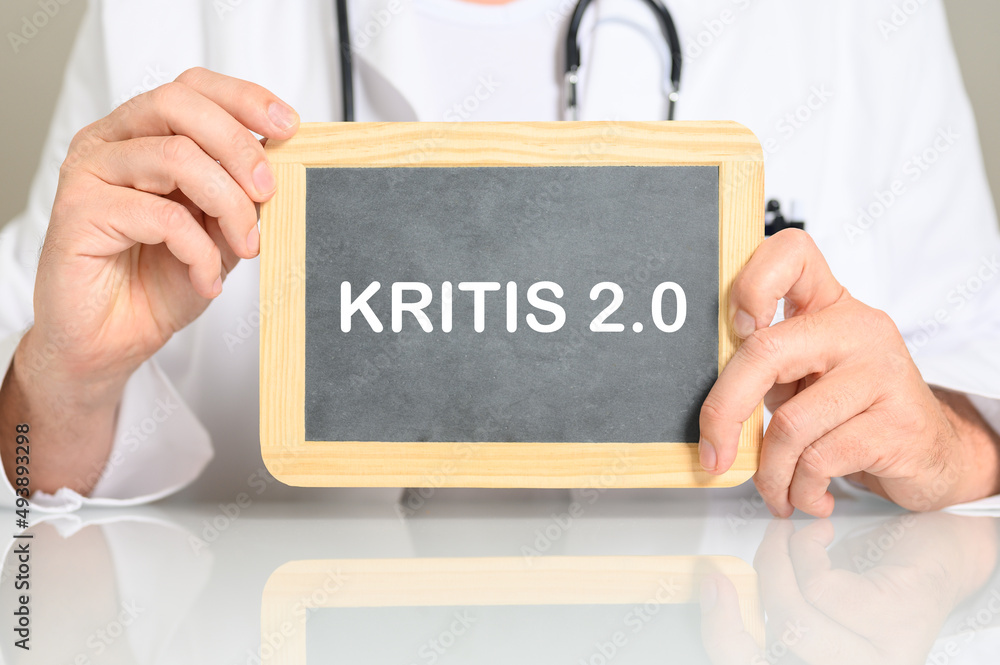 Ein Arzt am Schreibtisch mit einer Tafel auf der KRITIS 2.0 steht. Konzept Cyber Security für Krankenhäuser und Kliniken Ein Arzt am Schreibtisch mit einer Tafel auf der KRITIS 2.0 steht. Konzept Cyber Security für Krankenhäuser und Kliniken