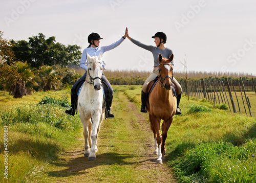 Youre doing great. Full length shot of two young woman high fiving while riding their horses on the ranch.