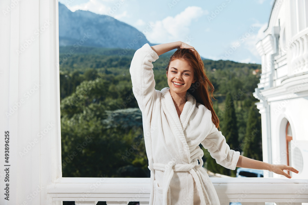 Portrait of gorgeous woman with long hair in a white bathrobe staying on the balcony in a hotel Perfect sunny morning - obrazy, fototapety, plakaty 