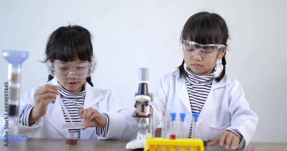 Slow motion shot, Two asian siblings wearing coat and clear glasses use microscope for experimenting with liquids, while studying science chemistry Slow motion shot, Two asian siblings wearing coat and clear glasses use microscope for experimenting with liquids, while studying science chemistry