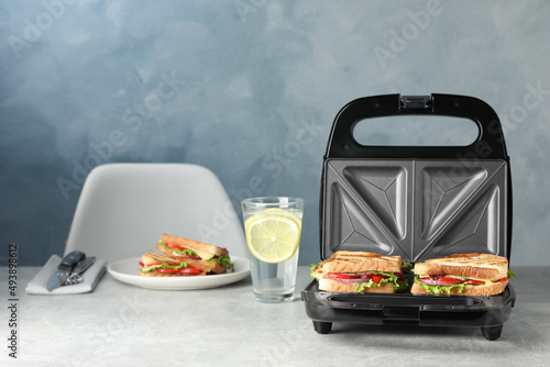 Modern grill maker with sandwiches and breakfast served on grey table