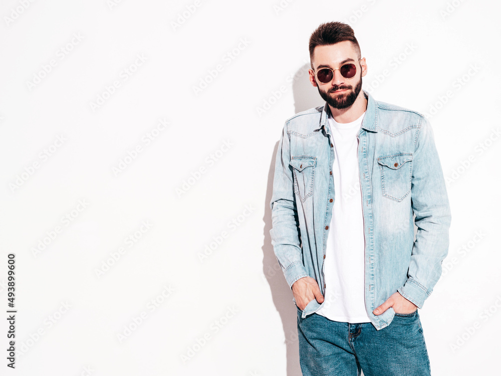 Portrait of handsome confident stylish hipster lambersexual model.Man dressed in jacket and jeans. Fashion male posing in studio in sunglasses. Isolated on white Portrait of handsome confident stylish hipster lambersexual model.Man dressed in jacket and jeans. Fashion male posing in studio in sunglasses. Isolated on white