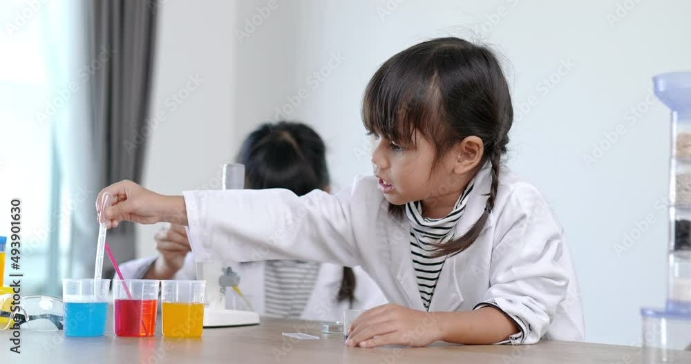 Front view Asian little girl wearing coat using dropper to suck liquid from glass beaker, blur three colors liquids in beakers, while studying science chemistry Front view Asian little girl wearing coat using dropper to suck liquid from glass beaker, blur three colors liquids in beakers, while studying science chemistry
