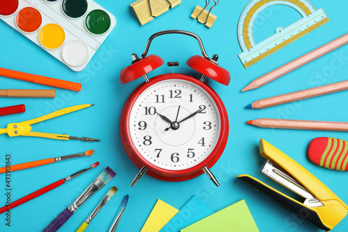 Flat lay composition with alarm clock and different stationery on light blue background. School time