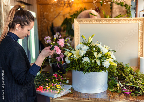 Cropped shot of a young woman florist arranging colorful flowers in a flower shop and making a bouquet. Florist woman creates flower arrangement in a round box. Beautiful bouquet of mixed flowers.