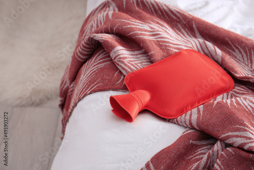 Red hot water bottle on bed indoors