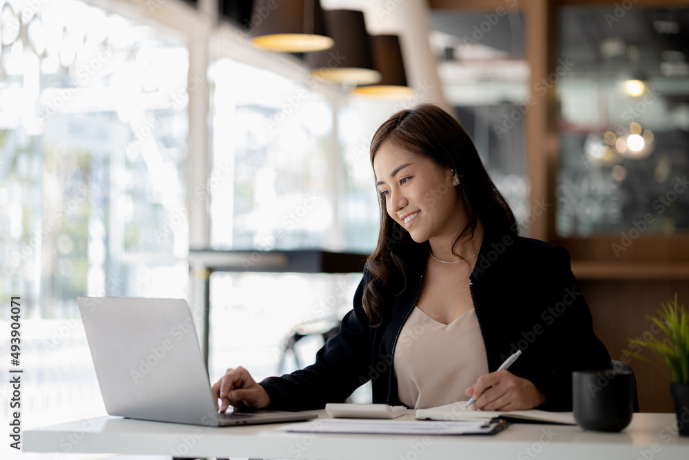 © kamiphotos - A beautiful Asian businesswoman sitting in her private office, she is checking company financial documents, she is a female executive of a startup company. Concept of financial management.