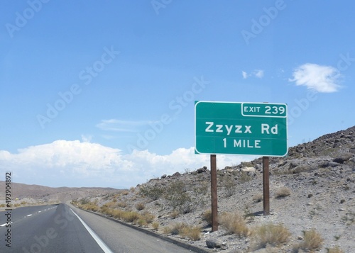 Roadside sign with distance and exit direction to ZZyzx Road along Interstate 15 in California.