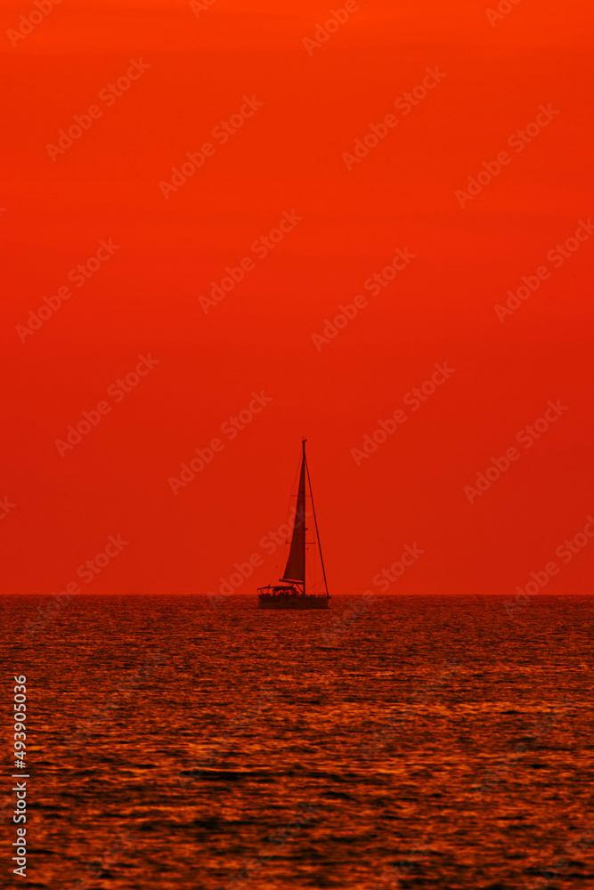 Silhouette of a sailing boat in sunset sunrise time and ocean horizon.