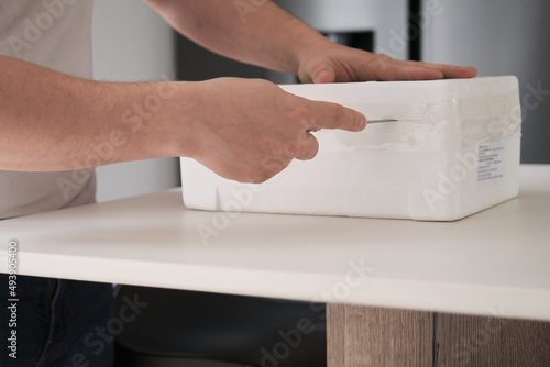 Close up of a man hands opening EPS isothermal box using a knife. photo