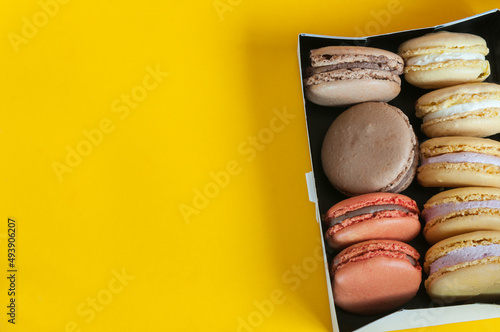 Multi-colored macaroons in a box on a yellow background. Top view, natural light. Selective focus with copy space