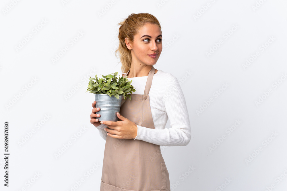 Young blonde gardener woman girl holding a plant over isolated white background thinking an idea Young blonde gardener woman girl holding a plant over isolated white background thinking an idea