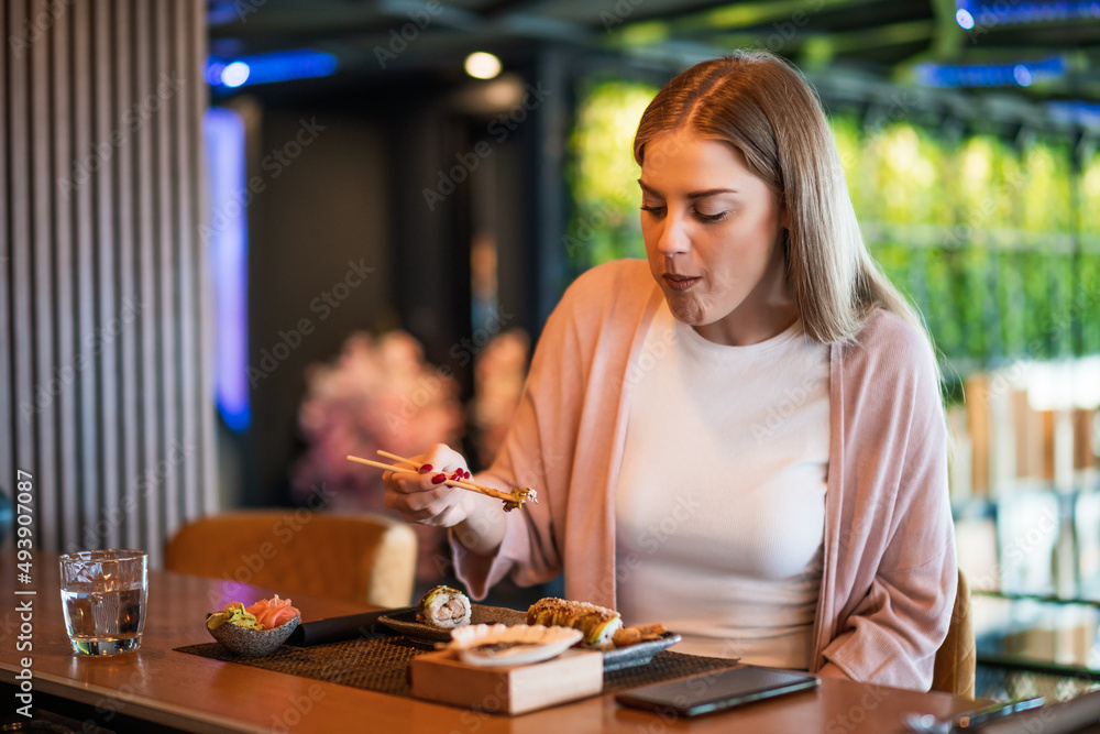 Young woman is eating sushi with chopsticks at sushi restaurant. Young woman is eating sushi with chopsticks at sushi restaurant.