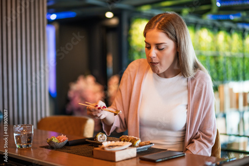 Young woman is eating sushi with chopsticks at sushi restaurant.