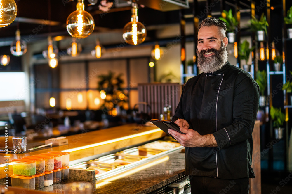 Portrait of sushi chef at sushi restaurant. He is receiving order on digital tablet. Portrait of sushi chef at sushi restaurant. He is receiving order on digital tablet.