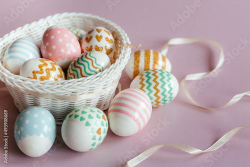 Easter eggs in pastel colors with a pattern in white basket on pink background.