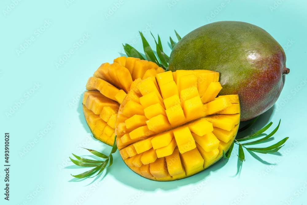 Summer background with mango and palm leaves. Fresh whole and sliced cut ripe mango fruit on bright turquoise background