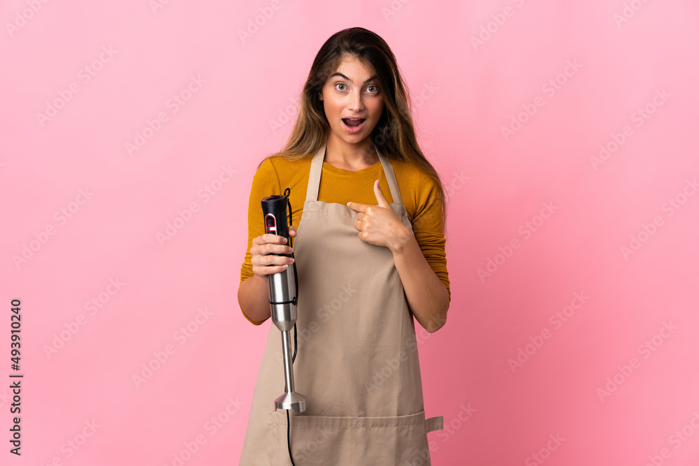 Young chef woman using hand blender isolated on pink background with surprise facial expression Young chef woman using hand blender isolated on pink background with surprise facial expression