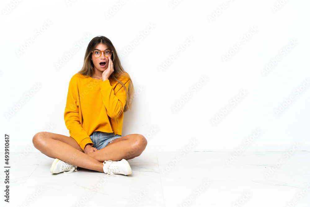 Young woman sitting on the floor isolated on white background with surprise and shocked facial expression Young woman sitting on the floor isolated on white background with surprise and shocked facial expression