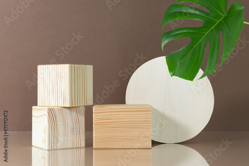 Fototapeta Naklejka Na Ścianę i Meble -  Wooden scenes on a beige table on a brown background with green monstera leaf. Premium podium for advertising your product. Background for the product presentation.