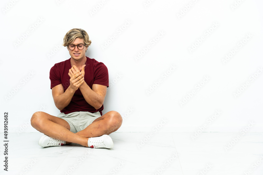 Fototapeta premium Young English man sitting on the floor suffering from pain in hands