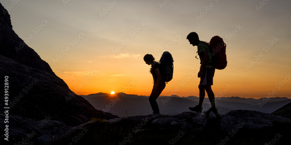 Silhouette of couple with backpack walking on mountain at sunset Silhouette of couple with backpack walking on mountain at sunset