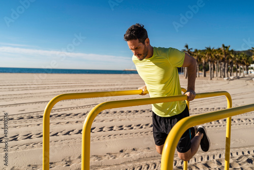 Athlete doing push ups on parallel bars at beach photo