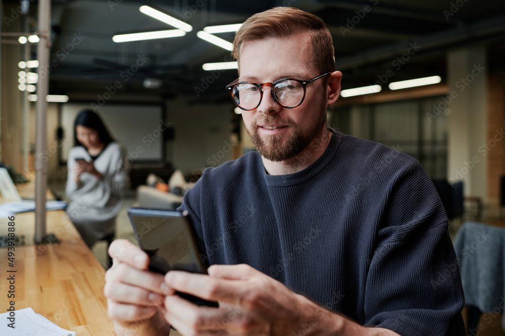 Smiling businessman with eyeglasses using smart phone at office Smiling businessman with eyeglasses using smart phone at office