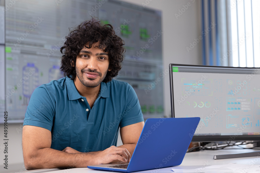Smiling technician with laptop at desk in control room