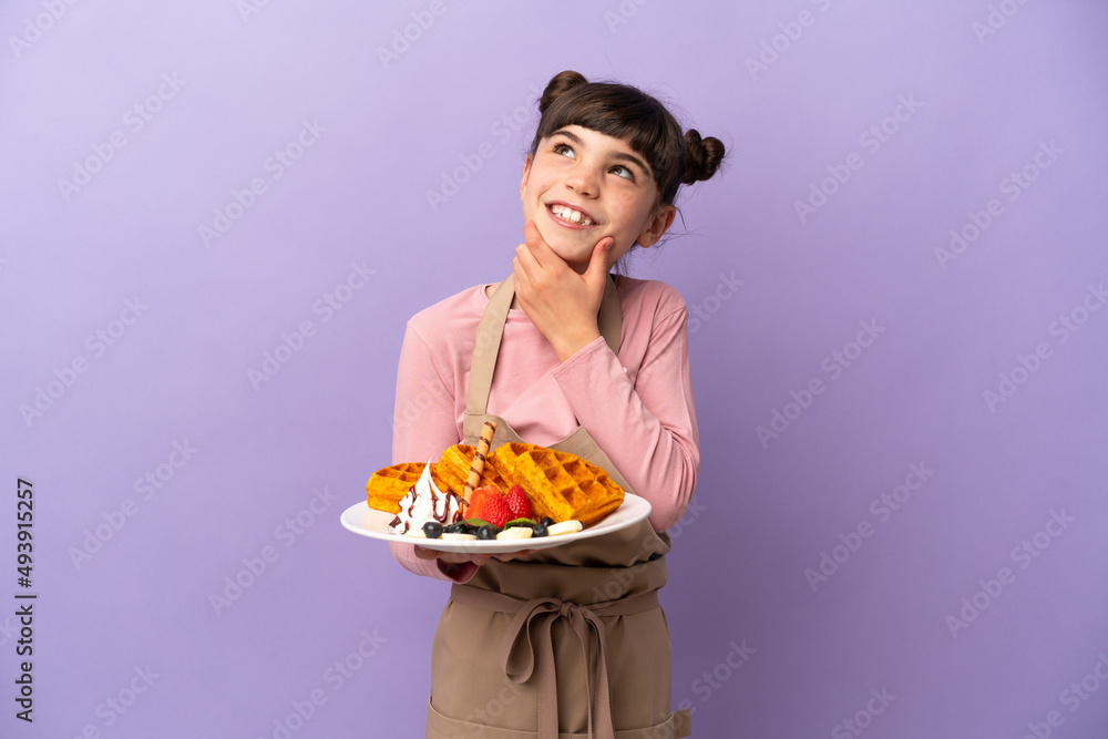 Little caucasian girl holding waffles isolated on purple background looking to the side and smiling Little caucasian girl holding waffles isolated on purple background looking to the side and smiling