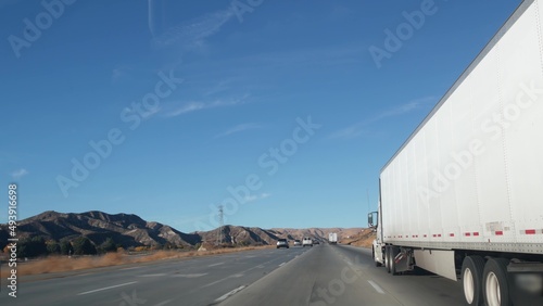 Lorry truck or semi-trailer on highway, freight cargo transportation in California USA. White container hauling or trucking on freeway road. Commercial transport logistics, van haulage. Cars driving.