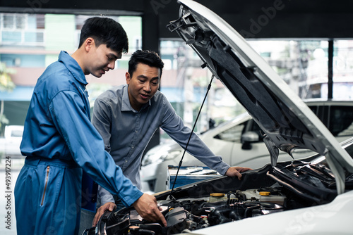 Asian automotive mechanic explain car condition to client in garage. 