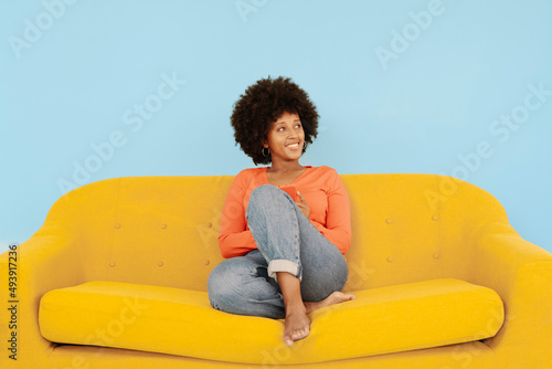 Happy woman sitting on yellow sofa in front of blue background photo