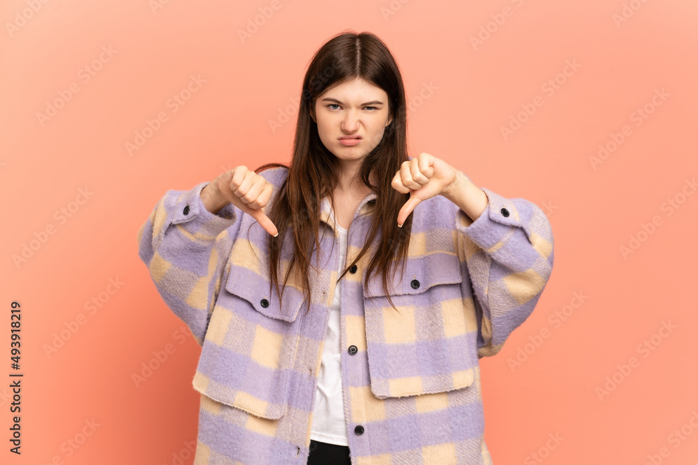 Young Ukrainian girl isolated on pink background showing thumb down with two hands