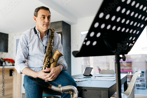 Musician sitting with saxophone looking at music stand in kitchen